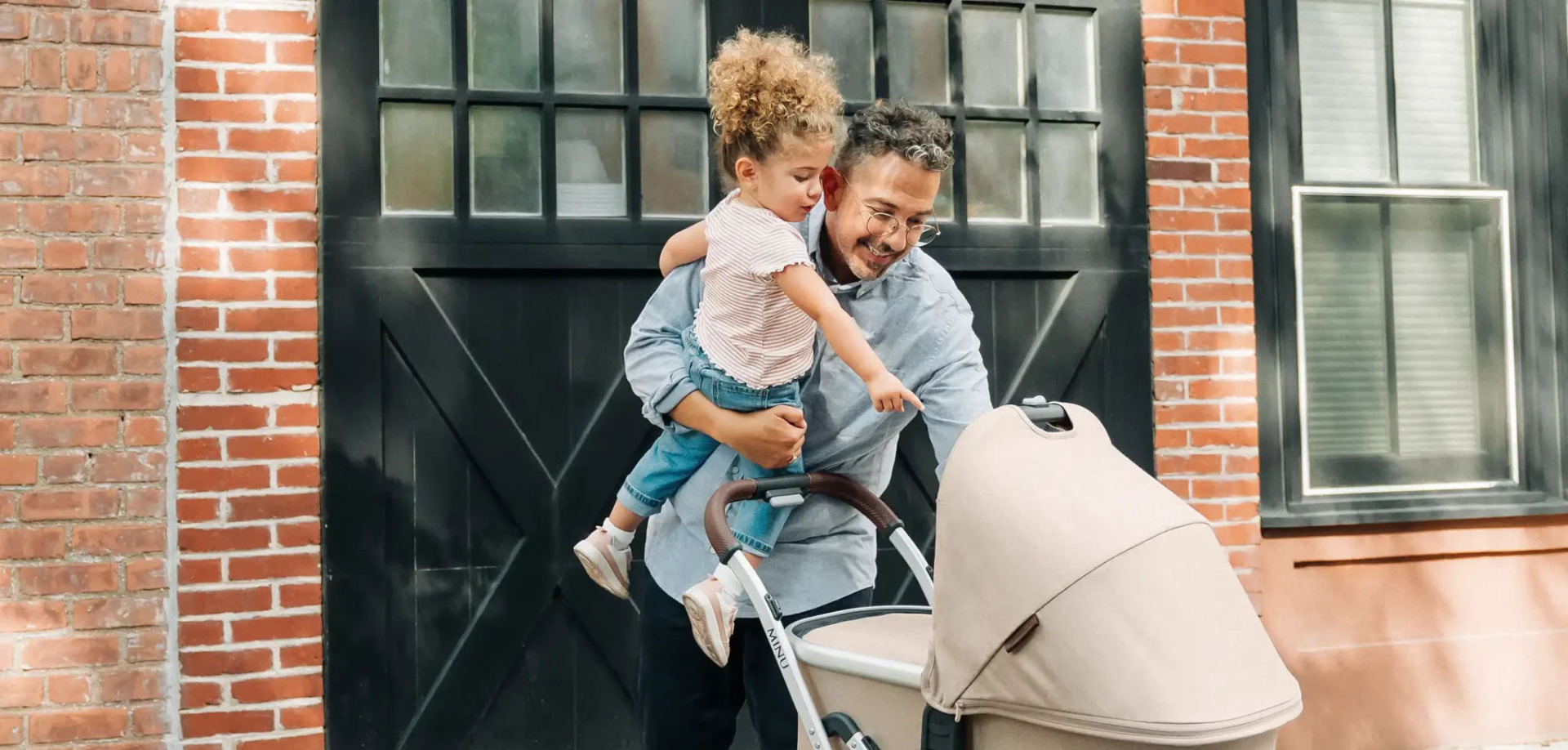 Parent carrying a child beside a compact UPPAbaby Minu stroller
